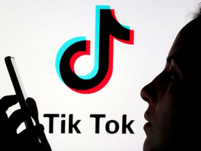 A person holds a mobile in front of the TikTok logo.