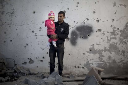 Un palestino sostiene a su hija junto a un edificio agujereado por munición y metralla por los ataques aéreos israelíes en la ciudad de Gaza.