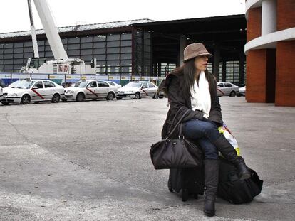 Una pasajera espera sentada sobre su maleta en la estación de Atocha, con una fila de taxis parados al fondo.