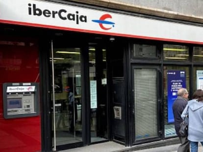 Tres personas pasan frente a una sucursal de Ibercaja.