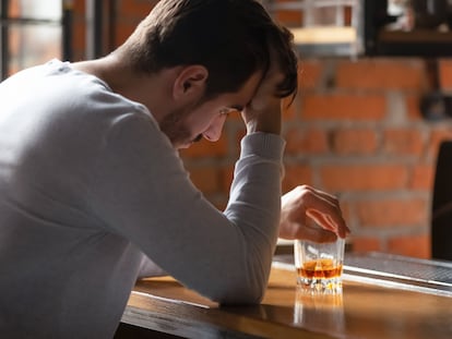 Un hombre sentado en un bar con un vaso de whisky.