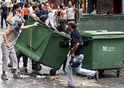 Un grupo de jvenes cruza un contenedor en la calle durante los disturbios por el desalojo de un centro <i>okupa</i> en Pamplona.