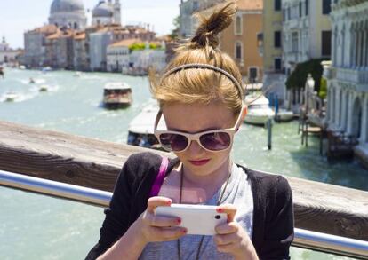 Una joven turista consulta su móvil en Venecia, con la cúpula de la iglesia de Santa María de la Salud al fondo.