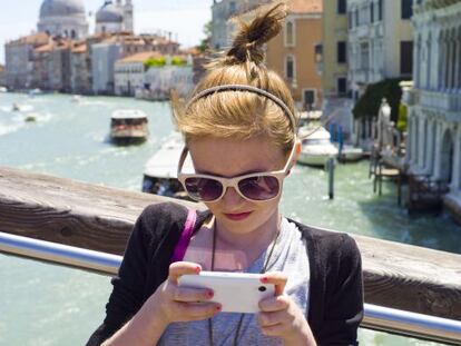 Una joven turista consulta su móvil en Venecia, con la cúpula de la iglesia de Santa María de la Salud al fondo.
