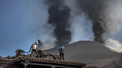 Dos vecinos retiran a pala la ceniza que cubre casi totalmente una casa en Las Manchas, en La Palma.