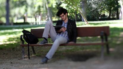 Un joven lector con su tableta sentado en un banco del parque del Retiro de Madrid.