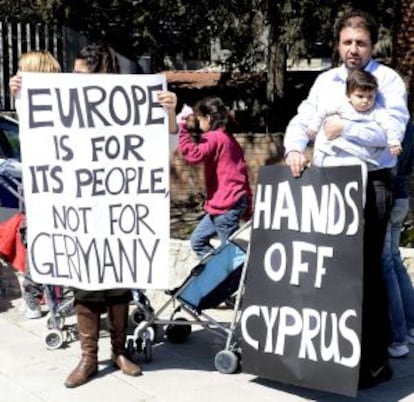 Un hombre sostiene una pancarta en la que se puede leer "mantened vuestras manos lejos de Chipre". A su lado, una mujer que sostiene otra en la que se puede leer "Europa es para su gente no para Alemania" frente al Parlamento en Nicosia (Chipre).