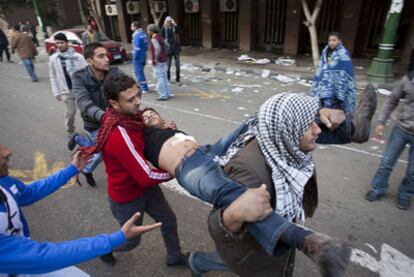 Varios manifestantes transportan a un herido durante los enfrentamientos con la policía ayer cerca de la plaza Tahrir de El Cairo.