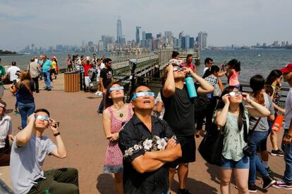 Várias pessoas assistindo ao eclipse do sol na Estátua da Liberdade, em Manhattan, nos EUA.