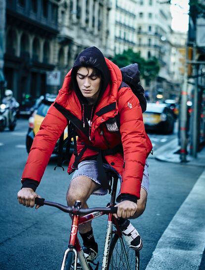 Plumífero rojo de Moncler, sudadera negra de Dior Homme, bermudas vaqueras de Replay y calcetines de Vans. La mochila y las zapatillas de ciclismo son del mensajero.