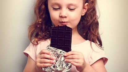 Una niña come una tableta de chocolate.