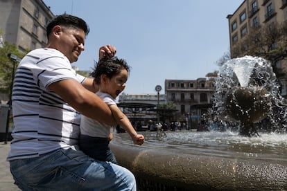 Un padre moja la cabeza a su hijo en las fuentes de la Plaza Universidad, en Guadalajara (Jalisco), el 15 de junio de 2023.