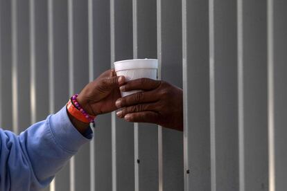 Un migrante de la caravana hondureña compra una taza de chocolate caliente a través de la valla de un refugio, en Tijuana (México).