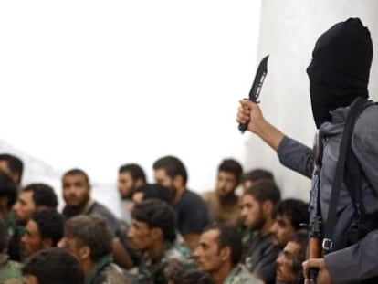 Un miembro del Estado Isl&aacute;mico blande un cuchillo junto a un grupo de soldados sirios capturados.