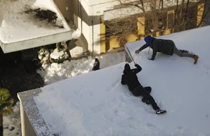 Una pareja limpia la nieve acumulada en una azotea de un edificio.
