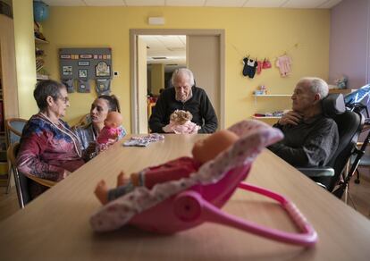 Imagem da sala de terapia ocupacional do centro. Ana Sanz dirige uma das sessões. Vários homens idosos contemplam as bonecas. Da esquerda para a direita, Mari Fe Lorente, Vicente Pérez e Salvador Castilla. Existem três daqueles que participam desta terapia. Todos os três estão em estágio moderado no avanço da doença.