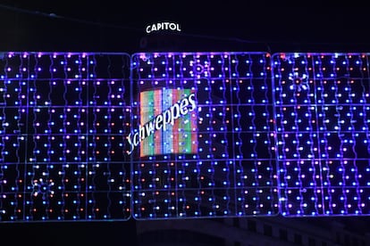 El icónico letrero de Schweppes en Callao, visto a través de las luces que cuelgan en Gran Vía. A los típicos arcos que cruzan de lado a lado las calles, se suman en toda la ciudad casi 6.700 cadenetas de luz, lo que equivale a unos 147 kilómetros, 118 cerezos y 13 grandes abetos luminosos.