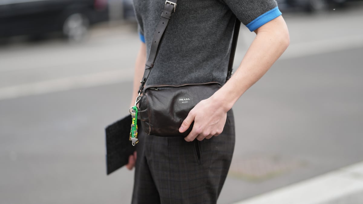 Un hombre luce un bolso de hombro de piel negra con detalles plateados.