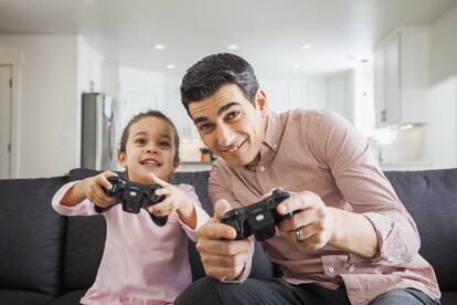 Un padre y su hija juegan a la consola en el salón de casa.