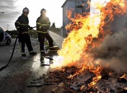 Dos bomberos apagan un fuego causado durante la jornada de huelga de ayer en un polígono de Puerto Real.