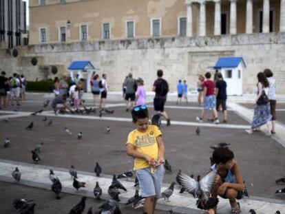 Un grupo de ni&ntilde;os juega con las palomas frente al edificio del Parlamento griego en Atenas