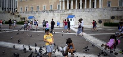 Un grupo de ni&ntilde;os juega con las palomas frente al edificio del Parlamento griego en Atenas