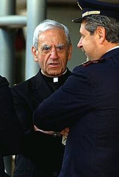 El cardenal Anthony J. Bevilacqua, de la Archidiócesis de Filadelfia, junto a un policía, espera una limusina tras llegar al aeropuerto de Fiumicino (Roma).