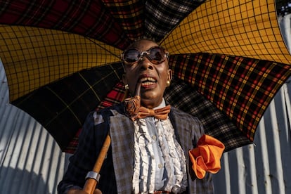Nkodia Aurelie, empresaria de 48 años y <em>sapeuse</em> durante 36, en Brazzaville en 2019. Viste traje de Negisom, camisa de Distingo, sombrero de Fin Mayser, gemelos de Min Min, reloj de Xonfa, pipa de fabricación local, paraguas de Faconable y zapatos de JM Weston.