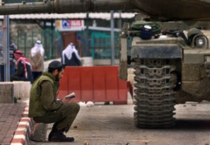 Un soldado israelí lee junto a un tanque.
