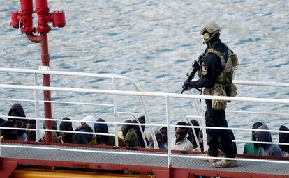 Un policía armado vigila a un grupo de inmigrantes a bordo del barco petrolero El Hiblu 1, en el Gran Puerto de La Valeta (Malta). Los inmigrantes, que habian sido rescatados en aguas del Mediterraneo y que iban a ser devueltos a Libia, secuestraron el barco para obligar al capitan a poner rumbo a Malta.
