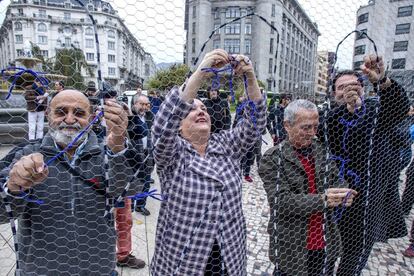 La cabeza de lista de EH Bildu al Congreso por Bizkaia, Onintza Enbeitia (centro), y el histórico dirigente Pablo Gorostiaga (i) colocan lazos morados en una red para conformar la palabra Bilbu, durante el acto que esta formación ha realizado esta mañana en Bilbao, en el que ha reunido a sus candidatos y candidatas al Congreso y al Senado por Alava, Bizkaia, Gipuzkoa y Navarra, para hacer un llamamiento para la manifestación del 6 de diciembre.