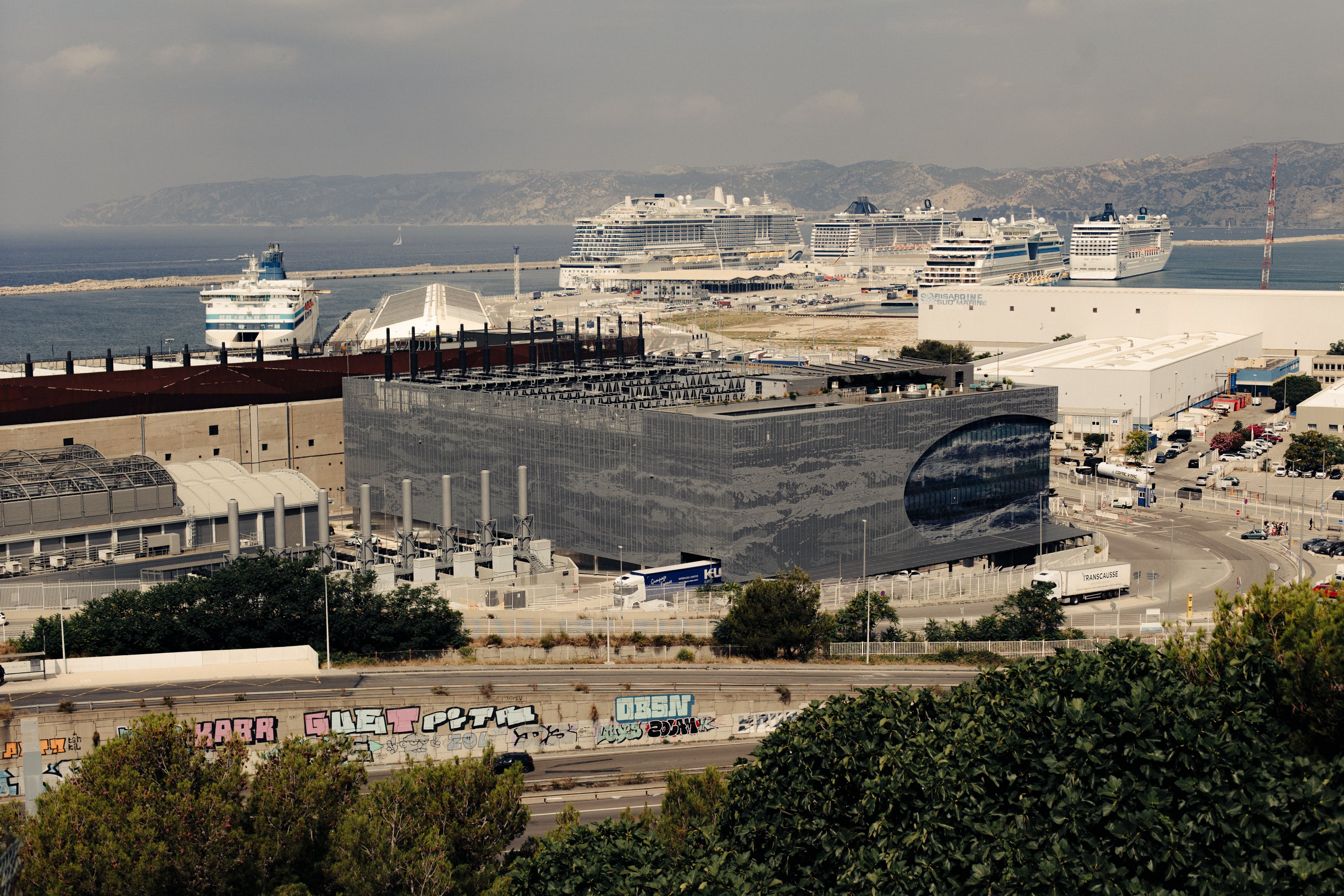 En primer término, los tres centros de datos que opera Digital Realty en el puerto de Marsella. Detrás, la terminal de cruceros, con cuatro buques amarrados, y un ferri.