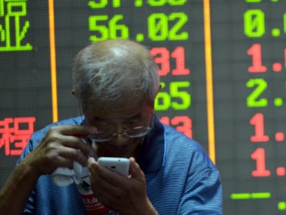 Un inversor examina su tel&eacute;fono m&oacute;vil ante un panel informativo de la Bolsa de Hangzhou (China).