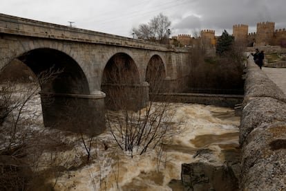 Un hombre toma imágenes del caudal del río Adaja. Al fondo, la muralla de Ávila.