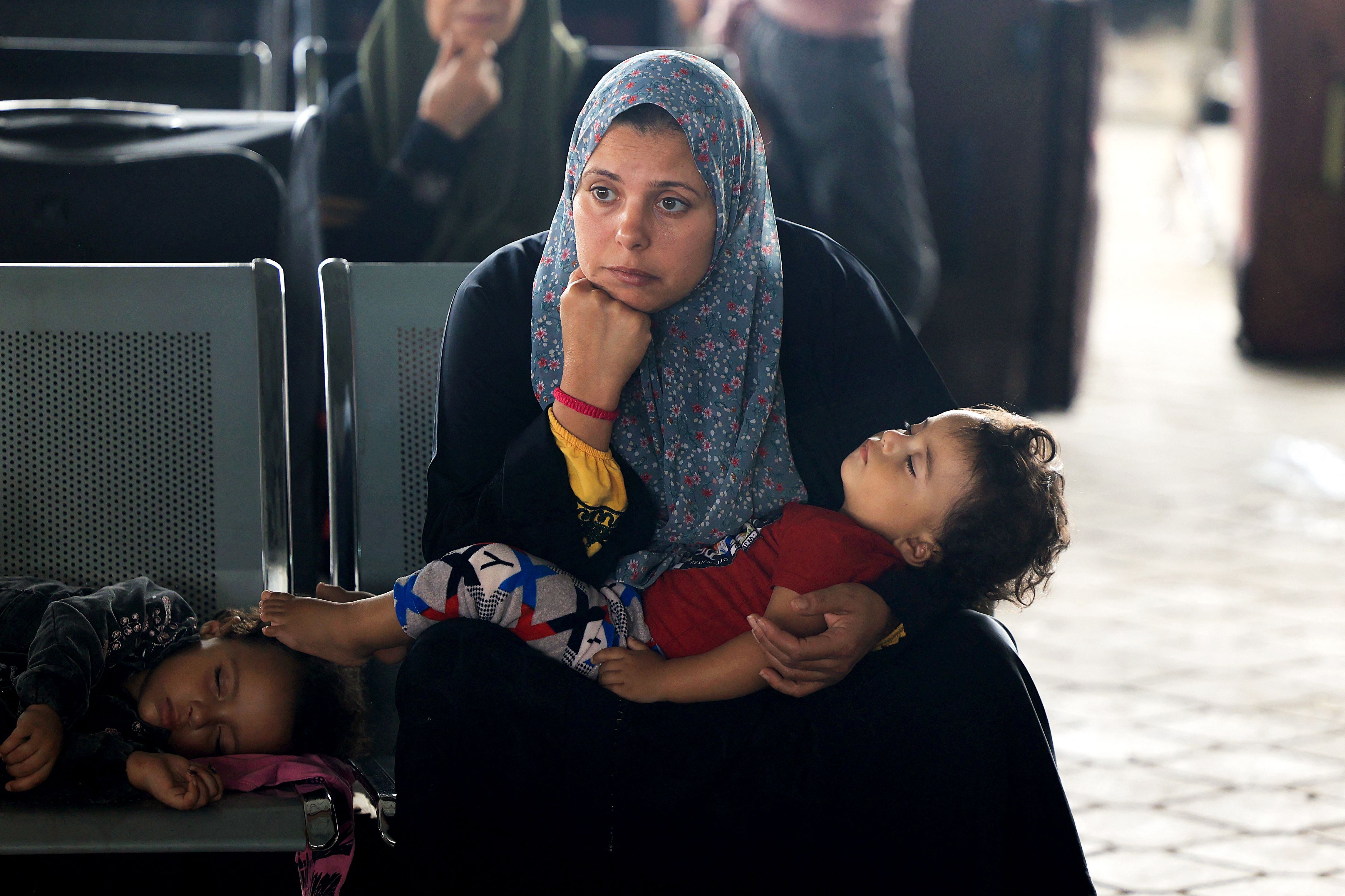 Una mujer junto con su hijo esperan para pasar por la frontera de Rafah con Egipto, al sur de la Franja, este jueves.