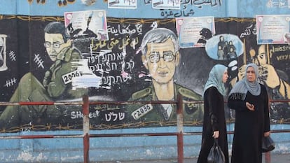 Mujeres palestinas caminan junto a un mural en el norte de Gaza en el que parecen imágenes del soldado Shalit en Gaza.