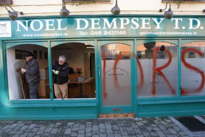Dos trabajadores reparan la cristalera de una oficina del Ministerio de Transportes en la localidad de Trim, asaltada y pintada con la palabra "Traidores".