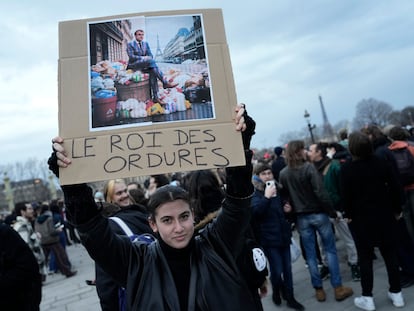 A woman holds a placard depicting French President Emmanuel Macron sitting on garbage cans that reads, "king of trash" during a protest in Paris, Friday, March 17, 2023.