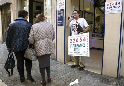 El dueño de la administración 'El Gato Negro', Miguel Ángel Jiménez (d), que ha vendido una serie del 22.654, el primer premio del sorteo extraordinario de la lotería de El Niño, sostiene un cartel con el número premiado que ha dejado dos millones de euros en Málaga capital.
