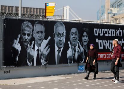 Dos israelíes pasan junto a un cartel de campaña de Yashar, que muestra al primer ministro Benjamin Netanyahu, al jefe del partido laborista Avi Gabbay, la presidenta del Meretz Tetz Zandberg, Benny Gantz y Yair Lapid sacando el dedo, en Jerusalén. 