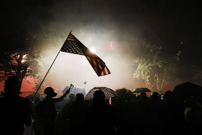 La policía de Estados Unidos utilizó gases lacrimógenos y pimienta durante las marchas de protesta la pasada madrugada en diferentes puntos del país contra el racismo y en medio de una ola de ira provocada por el despliegue de agentes federales ordenado por Donald Trump en las principales ciudades. En la imagen, un manifestante levanta la bandera de Estados Unidos durante una protesta antirracista frente al Palacio de Justicia Federal de Portland.