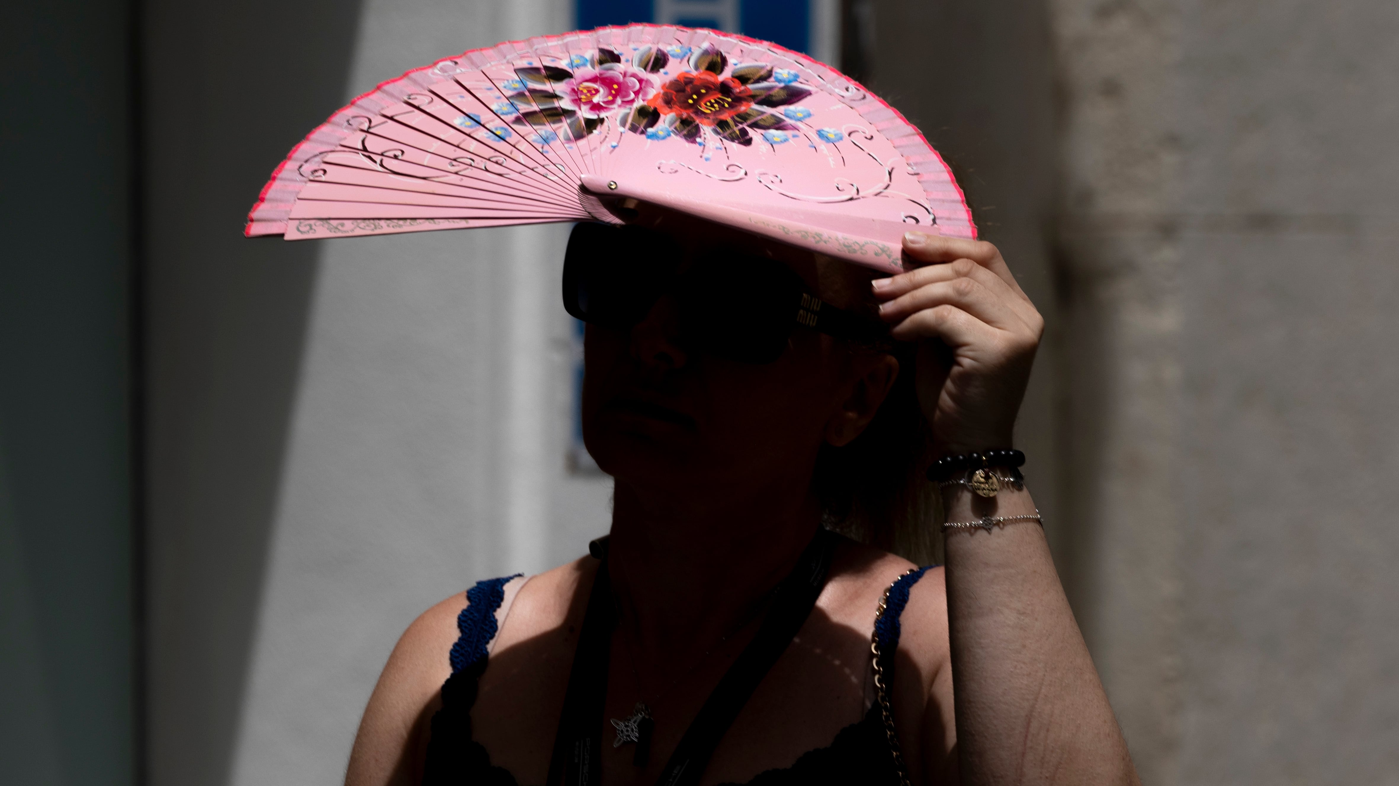 En la imagen, una persona con un abanico se protege del sol.