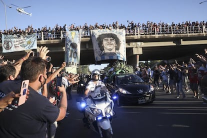 Cientos de aficionados saludan desde un paso elevado al coche fúnebre que lleva los restos de Diego Armando Maradona.