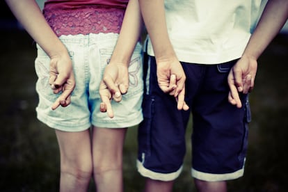 Dos hermanos, niña y niño, cruzan los dedos.