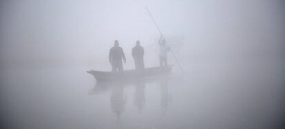 Gente en un bote alcanzando la orilla del río Rapti durante un mañana con una densa niebla en Sauraha (Nepal).