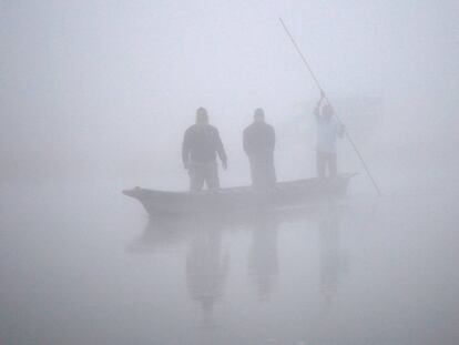Gente en un bote alcanzando la orilla del río Rapti durante un mañana con una densa niebla en Sauraha (Nepal).