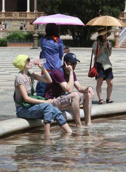 Una pareja de turistas se refresca en una fuente de la plaza de España de Sevilla.