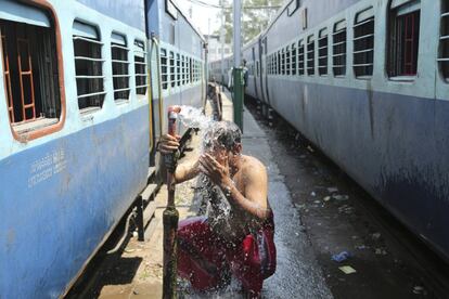 Un pasajero indio se baña junto a unos vagones de tren durante una tarde calurosa a las afueras de Jammu (India).