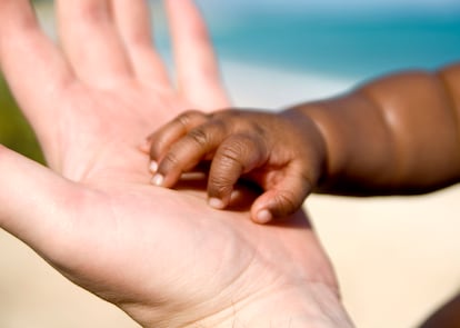 La mano de una persona adulta sostiene la de un bebé.