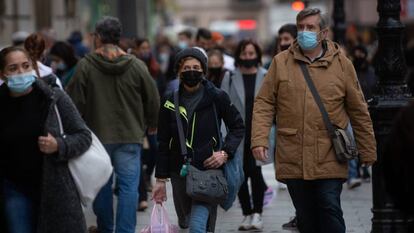 Viandantes caminan con bolsas por una vía de Barcelona.